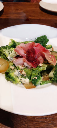 Salad with stroganina and broccoli on a white plate in a restaurantの写真素材