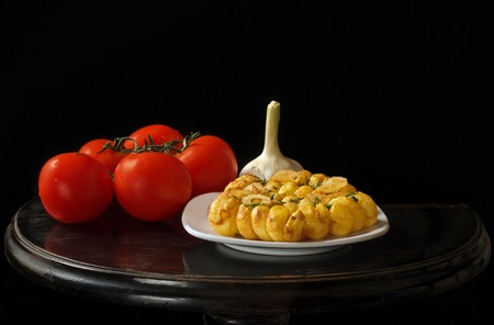 Roasted potatoes, garlic and tomatoes, black vintage table and black background.の写真素材