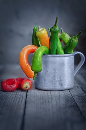 A beam of multi-colored chili in a Cup on the table out of old rough boards, and a gray background. Rustic style, defocused background.の写真素材
