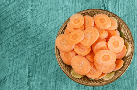 Sliced carrots in a bowl on wooden background. Tinted in blue-green color.の写真素材