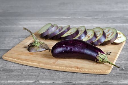 Eggplant lay on a cutting Board, on a gray wooden background.の写真素材