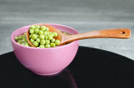 Green peas in a bowl and a wooden spoon. Old black surface and gray wooden background.の写真素材