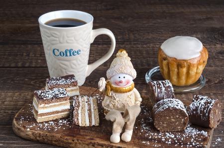 Variety of cakes dusted with powdered sugar, a toy Snowman and coffee mug with the inscription on the wooden surface.の写真素材
