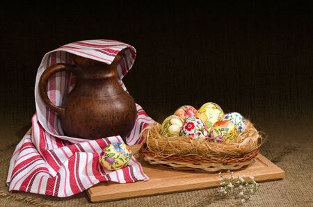 Decoupage Easter eggs in a basket and a jug under the towel, the dark background is burlap. Selective focus.の写真素材