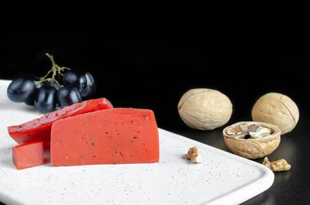 Red cheese, nuts and grapes on the Board. Selective focus, dark background