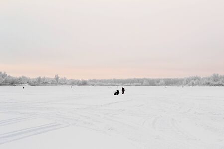 Natural winter landscape in frost, winter at dawn. Silhouettes of fishermen on a snowy river in the distance.の写真素材