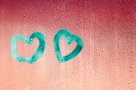 Aquamarine hearts drawn with a finger on wet red glass. The Concept Of Valentine's Day