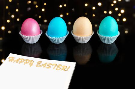 Multicolored Easter eggs on a black background with bokeh. The concept of a happy Easter. A piece of paper with space for textの写真素材