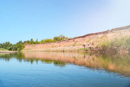 Summer river landscape with uninhabited steep Bank and blue sky