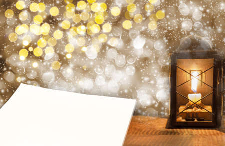 Delicate bokeh background with a candle in an old lantern and paper for text on a wooden surfaceの写真素材