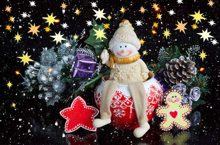 Toy snowman and Christmas decorations on a black background with snow and stars. Selective focus