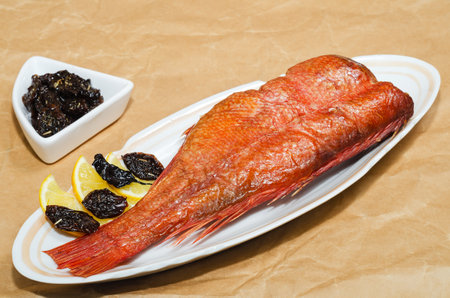 Hot smoked red sea bass with lemon and dried spicy plums, close-up on the background of crumpled...