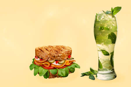 Big sandwich with ham, cheese, tomatoes, pickles and herbs. On a black background. Refreshing drink with ice and mint, light backgroundの写真素材
