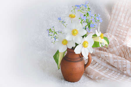 A small bouquet of anemones and forget-me-nots in a clay vase on a light backgroundの写真素材