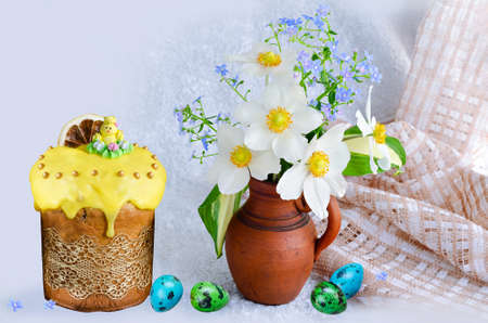 Glazed Easter cake decorated with sugar chicken and colorful quail eggs, a bouquet of anemones and forget-me-nots in a clay vase on a light background. Selective focusの写真素材