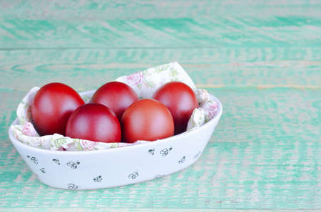 Red Easter eggs in a bowl, on an old background of boards painted in turquoise color. Selective focus, the concept of Easterの写真素材