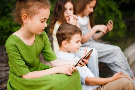 Children sit on the street and play with their smartphones.の写真素材