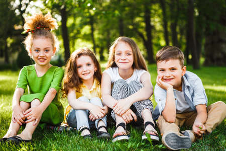 A group of children of school and preschool age are sitting on the green grass in the park.の写真素材