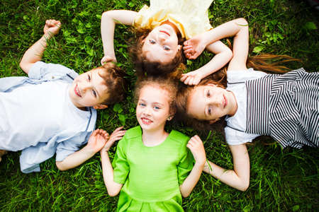 A group of kindergartners lies on the grass in the park smiling.