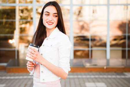 A girl is drinking coffee on the street near the showcase of a cafe.の写真素材