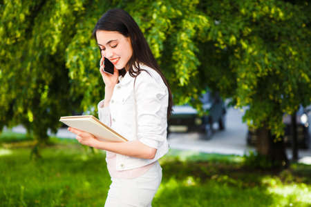 The girl is talking on the phone in the street with a notebook in her hands.の写真素材