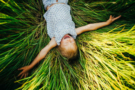 The girl lies on a big green glade and looks at the camera smiling. Top view.の写真素材