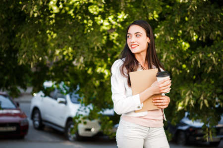 Beautiful girl with coffee and a notebook on a green summer street.の写真素材