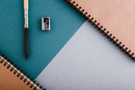 A pencil, a pencil sharpener and crafting notebooks on a green-gray background.