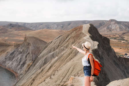 A girl in a straw hat and with an orange backpack walks along a ridge in the desert.の写真素材