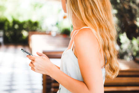 Blond girl sitting in a summer cafe with a cocktail and communicating on the Internet with a smartphone.の写真素材