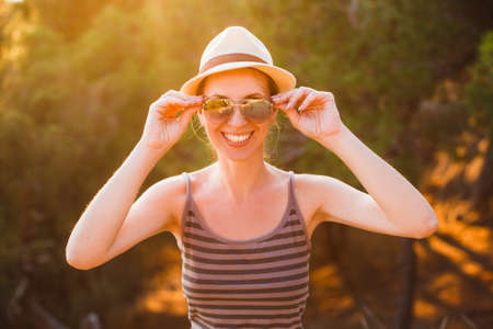 Outdoor close up portrait of young beautiful happy smiling woman wearing sunglasses, straw hat, posing in forest.の写真素材
