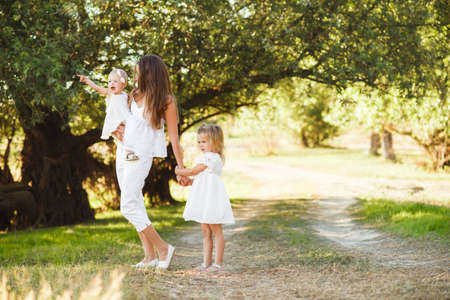 Mom with two little daughters are walking among the beautiful green forest.の写真素材