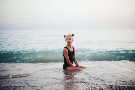 A teenage girl is sitting on the beach in a black swimsuit.の写真素材
