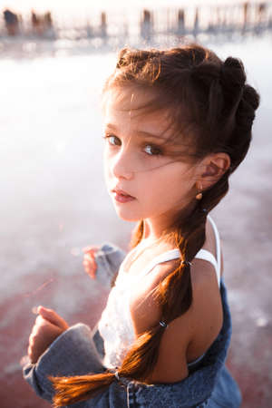 young girl in jean jacket and pony tails being imaginiate against the background of the ocean and...