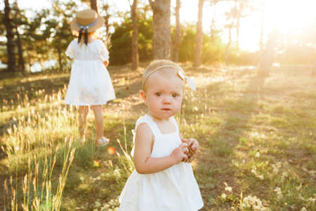 Children in white clothes and straw hats walk in the warm autumn forest.の写真素材