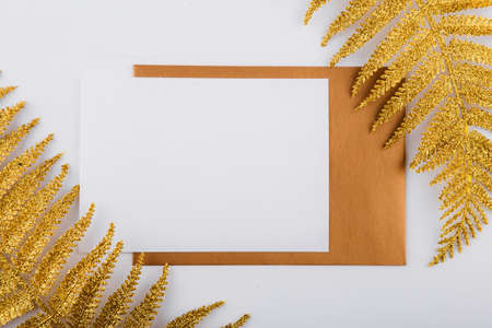 Mockup white greeting card and envelope with golden fern leaves and light background.の写真素材