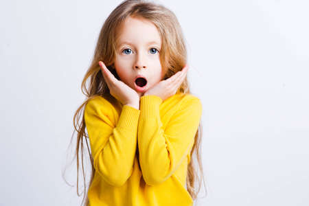 Close up portrait of surprised happy little girl,with long blond hair in a yellow sweater.