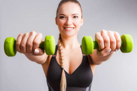 Beautiful young woman doing exercises with dumbbells. Photo athletic woman with perfect body on white background. Strength and motivationの写真素材