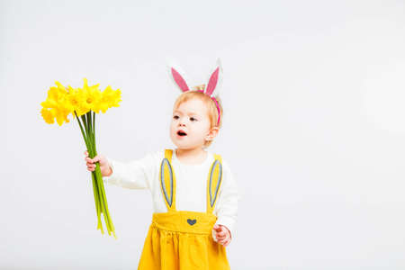 Smiling cute baby child in rabbit costumewith a bouquet of yellow daffodils on a white background.