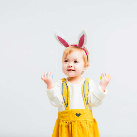 Smiling cute baby child in rabbit costumewith a bouquet of yellow daffodils on a white background.