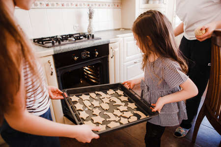 The little daughter in the chefs hat and apron and her mother prepare baking in the bright, classic...