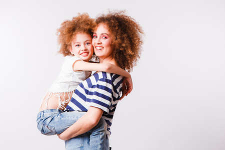 Mom and daughter with natural small curls on the head on a light background.の写真素材