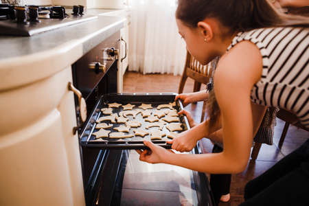 The little daughter in the chefs hat and apron and her mother prepare baking in the bright, classic kitchen.の写真素材