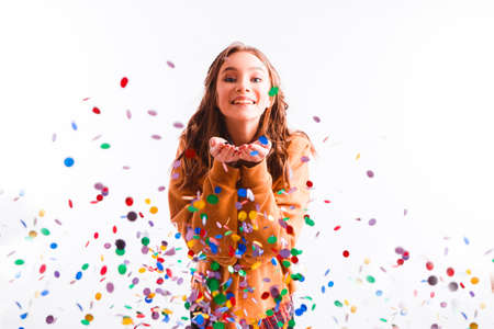 Cute teen girl on a light background throws color candy. Party concept.