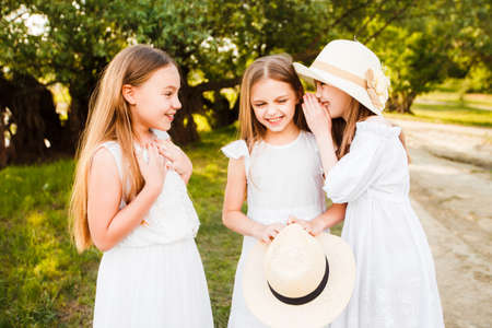 Three girls in white dresses walk in nature in the summer. Childrens pastime during the summer...
