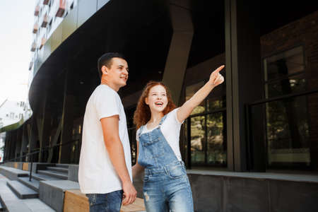 A young couple is walking in the modern city, holding hands. Inspect the conceptual archeology.