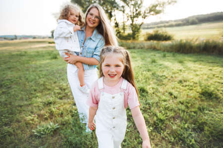 Blonde mother with two cute daughters are walking and having fun outdoors. Stylish, casual clothes.の写真素材