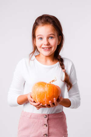 A beautiful girl on a light gray background is fooling around and grimacing with small pumpkins for a Halloween.の写真素材