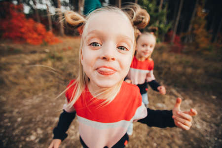 Twin blondes walk and have fun in the autumn forest among the red trees.