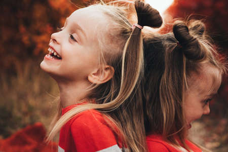 Twin blondes walk and have fun in the autumn forest among the red trees.の写真素材